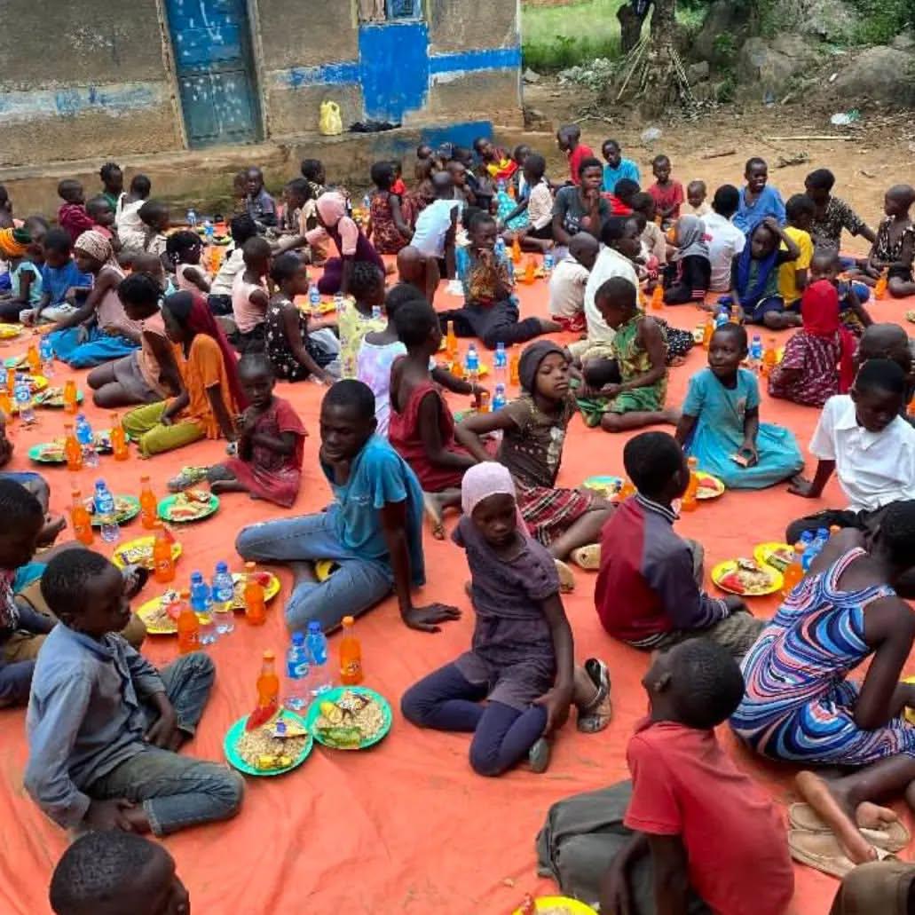 Large group of children and adults sharing a communal meal during feeding program